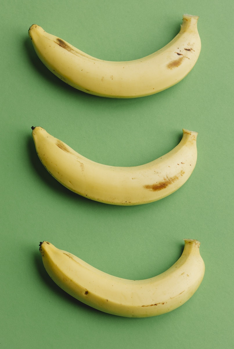 Top view composition of healthy ripe bananas with dark spots arranged in row on green background